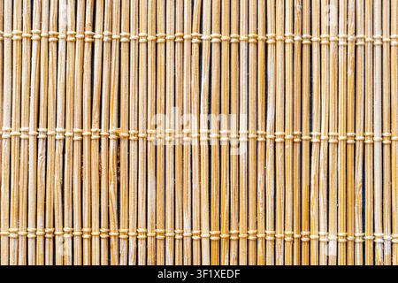 A close-up shot of a bamboo mat shows thin, vertical bamboo sticks bound together by horizontal threads. The natural color and texture of the bamboo c Stock Photo