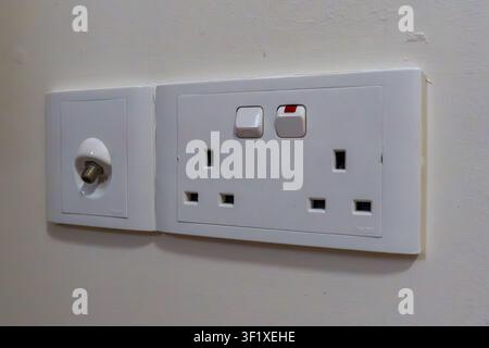 White wall-mounted electrical socket with switch and plug outlets. Single round socket cover visible beside the unit. Simple, clean design with no vis Stock Photo