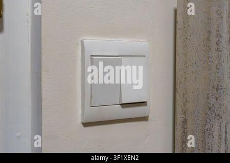 White light switch mounted on textured wall. Switch plate shows slight wear and age. Wall texture contrasts with smooth switch surface. Simple, functi Stock Photo