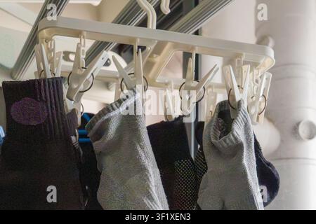 Colorful socks hang drying on a white plastic rack. Soft fabric textures contrast with clean, simple background. Socks vary in pattern and shade, crea Stock Photo