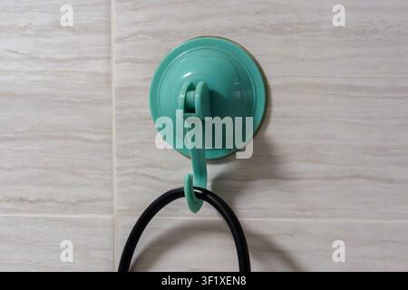 Green suction cup hook attached to tiled wall. Black cord hangs from the hook. Simple, functional, and practical design. Ideal for bathroom or kitchen Stock Photo