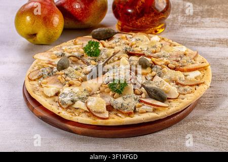 Freshly baked flatbread topped with sliced pears, blue cheese crumbles, pine nuts, capers, parsley, drizzled with honey, served on a wooden board with Stock Photo