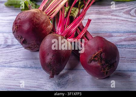 Vibrant red beetroots with green stems arranged on weathered wood. Natural lighting highlights deep purple hues and earthy texture. Ideal for food, he Stock Photo