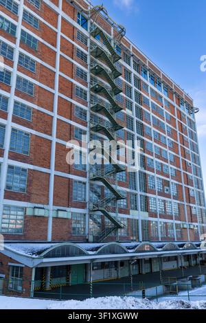 Large red brick building featuring many windows and a visible fire escape structure Stock Photo