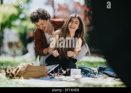 Young students laughing together outdoors while studying chemistry models on a park picnic Stock Photo