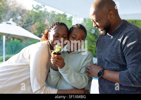 African American family on covered patio, daughter in hoodie holding potted seedling, smiling Stock Photo