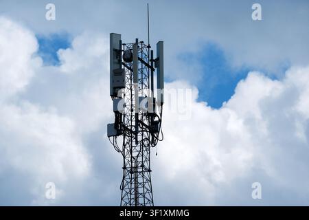 Close-up of a cellular communication tower equipped with multiple antennas and wireless transmission equipment against a dramatic cloudy sky, represen Stock Photo