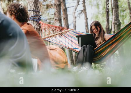Young woman using a laptop in a colorful hammock while relaxing outdoors in a forest park Stock Photo