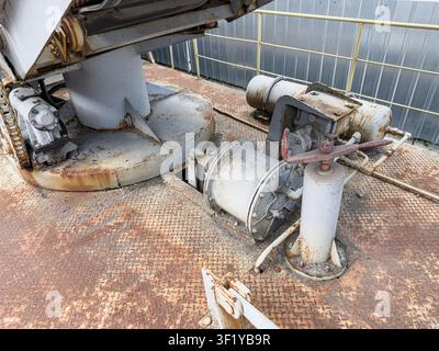Railroad equipment featuring cylindrical component with valve and piping on a worn metal platform, corrugated wall in the background, muted earth tone Stock Photo