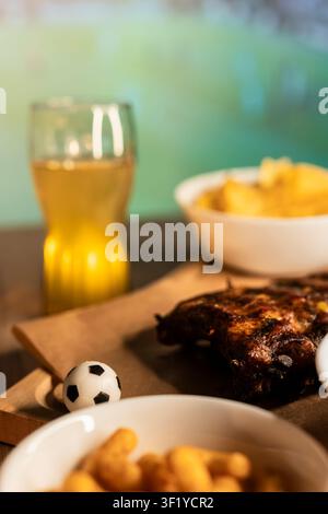 Grilled ribs on a wooden board with beer and snacks, highlighting a soccer viewing party atmosphere with barbecue. Stock Photo