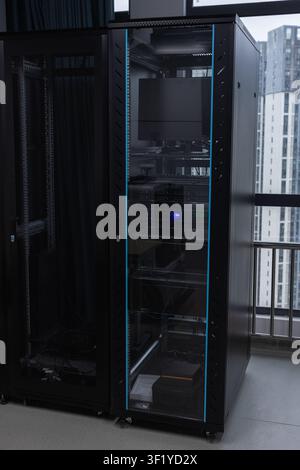 Glass-doored server rack in a modern office data center housing rack servers, monitor and cabling. Dimly lit IT equipment conveys technology, connecti Stock Photo