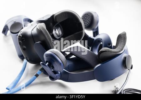 Blue virtual reality headset paired with controllers and integrated over-ear headphones, ideal for immersive gaming, simulation, and tech demos. Close Stock Photo