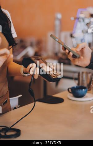 Asian senior female barista adult receiving mobile payment from customer using smartphone at cafe demonstrating modern cashless transaction in cozy lo Stock Photo