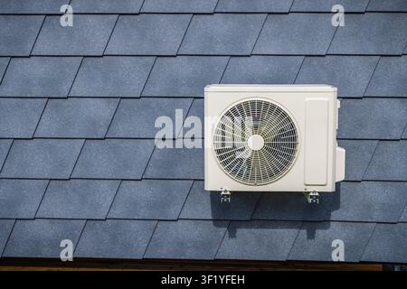 Outdoor air conditioning split unit mounted on a dark gray diamond-shaped shingle wall Stock Photo