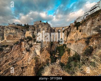 View of the iconic Puente Nuevo bridge spanning the deep El Tajo gorge, with historic white buildings perched on the cliff edge under a dramatic cloud Stock Photo