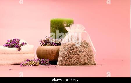 A spa-inspired composition features a green candle surrounded by lavender in a wooden bowl, a stack of white towels Stock Photo