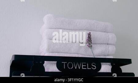 A vibrant purple lavender sprig rests on a pristine stack of white towels, with a black metal shelf featuring Stock Photo