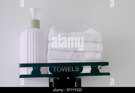 pump bottle, stands beside a stack of white towels on a black metal shelf adorned Stock Photo