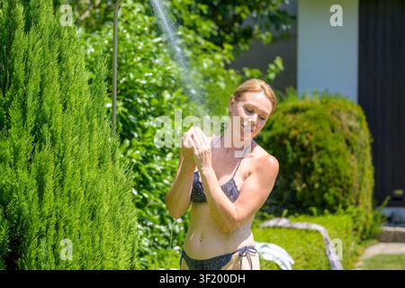 Woman enjoying a refreshing outdoor shower in the garden while cooling down during a hot summer day. Stock Photo