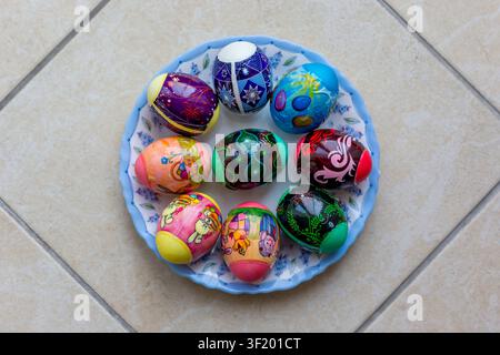 Colorful decorated easter eggs arranged in a blue bowl on tiled floor Stock Photo