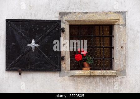 147 Red pelargonium in the barred, black iron shuttered, open window of the XVII c.Martinova hisa on Mestni trg square west side. Skofja Loka-Slovenia Stock Photo