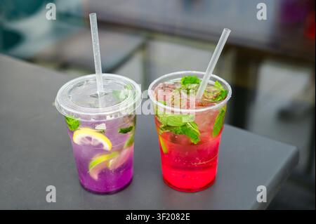 Two refreshing homemade lemonades served in plastic takeaway cups with ice, fresh fruit and mint. Cold summer beverages and outdoor refreshment. Stock Photo