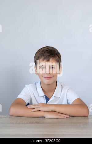 Smiling schoolboy portrait with folded arms at desk, calm posture, short brown hair, blue eyes Stock Photo