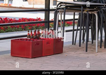Empty beer bottles in red crates are waiting for collection on a sidewalk patio Stock Photo