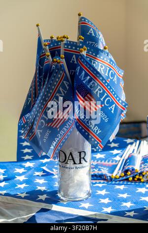 Small blue America 1776-2026 flags with gold tips fill a glass vase on a patriotic star-themed table setting. Stock Photo