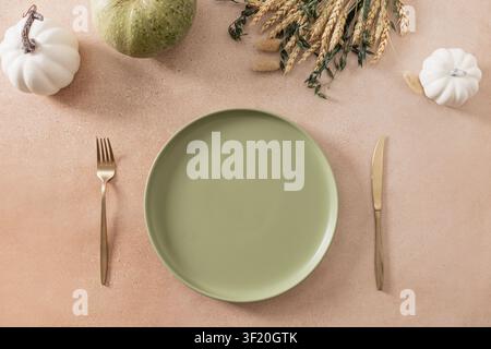Seasonal autumn table setting with green ceramic plate, decorative pumpkins, dried wheat and elegant cutlery. Thanksgiving dining concept with copy sp Stock Photo