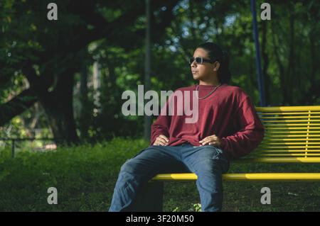 Young man wearing sunglasses sitting on a park bench. Man wearing sunglasses sitting in the park Stock Photo