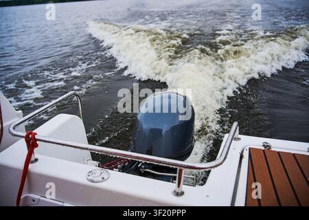 Trail of water behind a fast motorboat on the lake. Dynamic wake left by an outboard boat engine. Close up of the rear deck and motor of a pleasure bo Stock Photo
