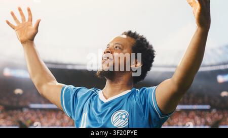 African american football player in blue jersey cheering and saluting fans, entering stadium pitch before game. Determined footballer showing team spirit, pre-match under stadium light. Stock Photo