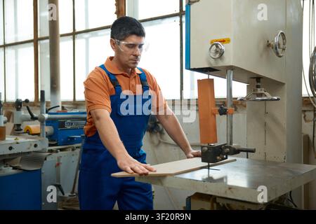 Skilled carpenter using bandsaw to shape curved panel while maintaining safety precautions and focus Stock Photo