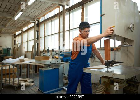 Skilled carpenter using bandsaw to shape curved panel while maintaining safety precautions and focus Stock Photo