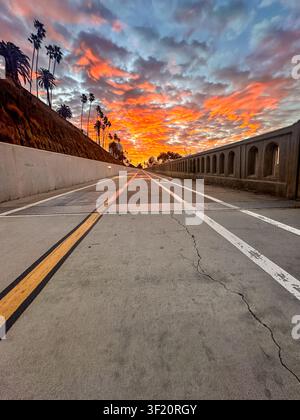 Dramatic sunrise sky over the California Incline in Santa Monica, with palm trees silhouetted against fiery orange and pink clouds, California, USA Stock Photo