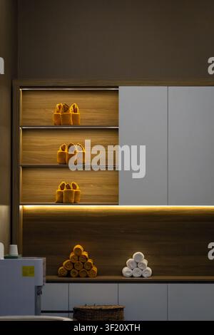 Neatly arranged spa shelves with slippers and rolled towels in warm Phu Quoc resort lighting Stock Photo