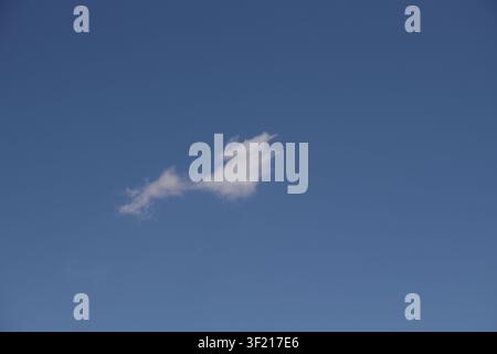 A solitary delicate white cloud floats in a boundless bright blue sky representing peace and freedom during a clear summer day single wispy vastness d Stock Photo