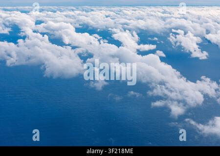 Soft white clouds drift above a vast blue ocean, forming gentle patterns that stretch toward the horizon. Scene evokes calm and endless freedom beneat Stock Photo