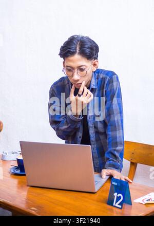 Focused young Asian man concentrating on his laptop while working remotely at a coffee shop, lifestyle portrait. Stock Photo