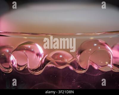 Macro abstract photography of a wavy glass rim with soft pink and purple liquid illumination Stock Photo