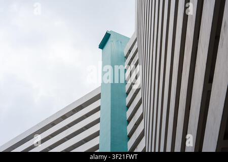 Modern building features bold geometric lines and a striking teal accent. Striped facade contrasts with smooth, painted architectural surfaces. Sky pr Stock Photo