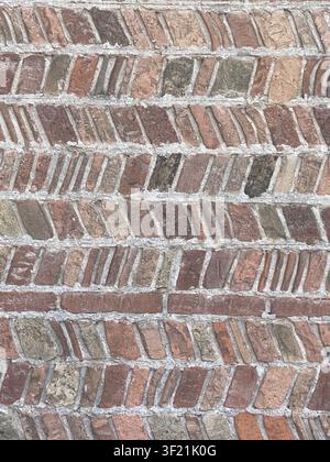 Varied old bricks form a striking herringbone bond on an exterior wall, showcasing weathered surfaces and distinct mortar lines, perfect as a textured Stock Photo