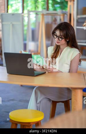 Asian businesswoman reading reports while using laptop in a stylish natural interior office. Stock Photo