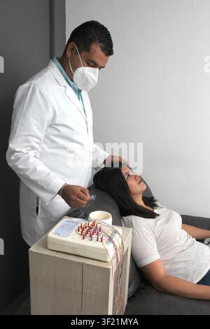 Latin neurologist medical specialist doctor measures the head of his Latin woman patient to stick the electrodes and check the brain activity Stock Photo