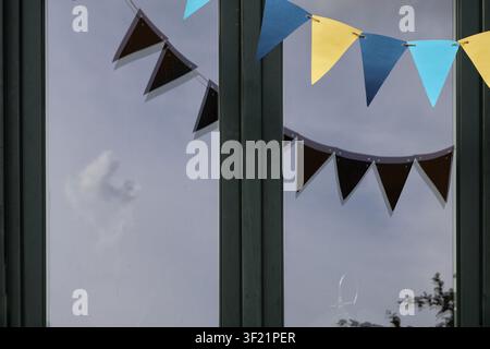 Colorful Bunting Reflected in Modern Glass Window with Cloudy Sky – Festive Abstract Architectural Detail Stock Photo