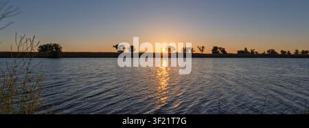 Panoramic sunset over a tranquil, deep blue river Stock Photo