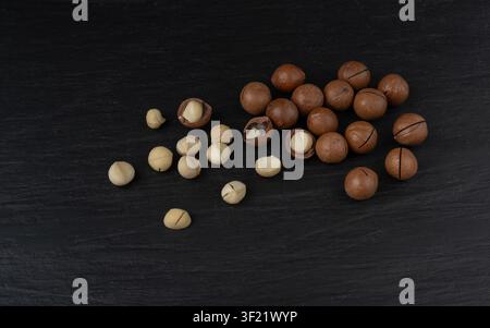 Macadamia nuts scattered. Natural raw peeled macadamia seeds and shells, the hardest and most expensive nuts in the world on black background Stock Photo