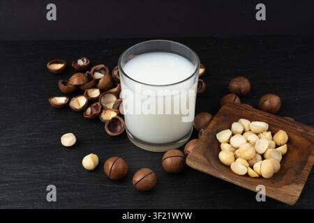Macadamia nuts milk in glass. Natural raw peeled macadamia seeds and shells, the hardest and most expensive nuts in the world on black background Stock Photo