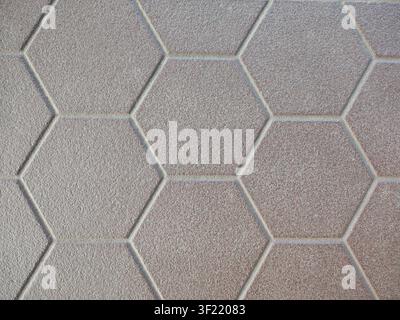 surface is laid with hexagonal tiles in a gray-beige color with a matte, rough texture. Clear, light-colored grout creates a geometric honeycomb block Stock Photo
